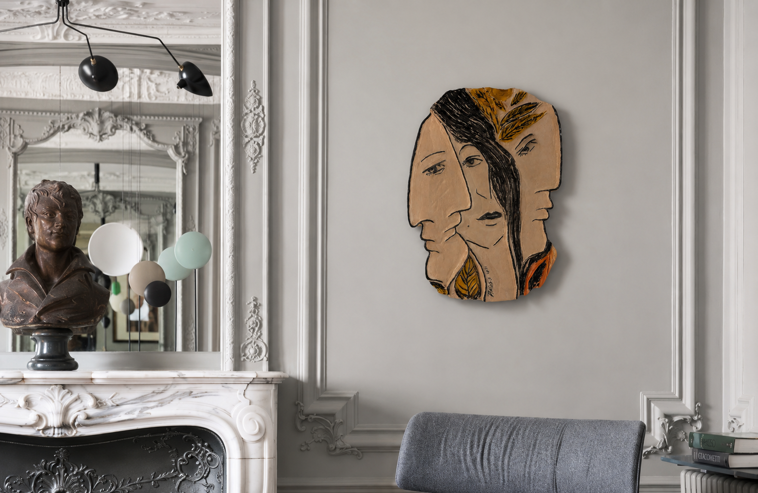 Trois visages encadrée dans une boiserie classique au-dessus d'un fauteuil gris, près d'une cheminée en marbre