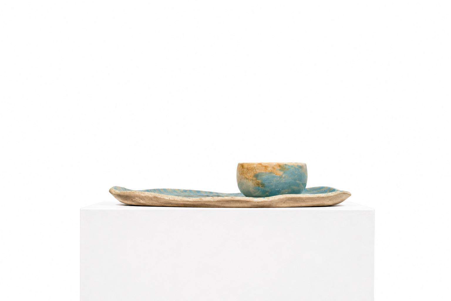 Plat au visage bleu présenté sur un socle blanc en galerie